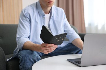 Man with passport using laptop at table indoors, closeup