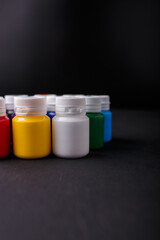 Small bottles of multicolored acrylic or gouache paint jars in a box on dark background. Art materials. Copy space