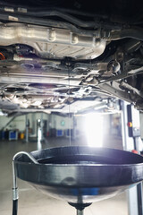 Dirty old motor oil dripping from car engine into container in workshop, closeup