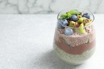 Delicious chocolate pudding with chia seeds, kiwi, mint and blueberries in glass on grey textured table against marble background, closeup. Space for text
