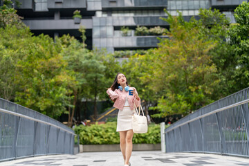 Asian woman holding coffee cup walking to work in urban morning professional office background,...