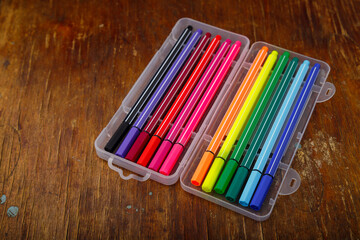 Multicolored marker or fine liner pens in plastic case on wooden table background. Art tools
