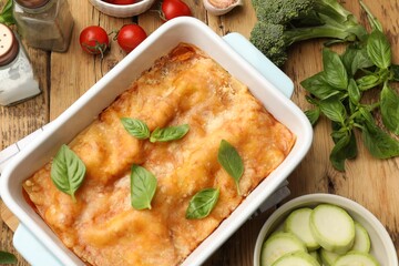 Tasty vegetarian lasagna in baking dish and ingredients on wooden table, flat lay