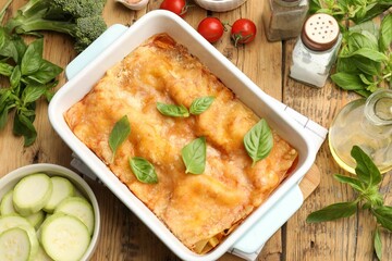 Tasty vegetarian lasagna in baking dish and ingredients on wooden table, flat lay