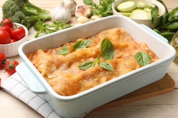 Tasty vegetarian lasagna in baking dish and ingredients on white wooden table, closeup