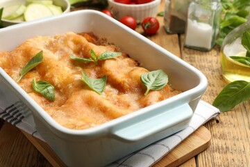 Tasty vegetarian lasagna in baking dish and ingredients on wooden table, closeup