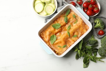 Tasty vegetarian lasagna in baking dish and ingredients on white table, flat lay. Space for text