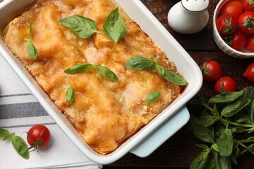 Tasty vegetarian lasagna in baking dish and ingredients on wooden table, flat lay