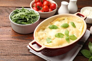 Tasty vegetarian lasagna and ingredients on wooden table, closeup