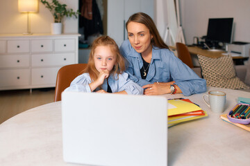 Young schoolgirl with her mother reading electronic resource for homework
