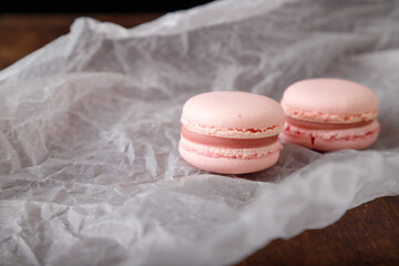 Tender pink macaroons on paper, wooden background. Forest berries, strawberry or raspberry flavor....
