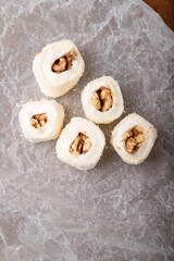 Turkish delight, white locum roll with walnut and coconut flakes on white paper, wooden background. Eastern sweets, oriental food. Traditional dessert