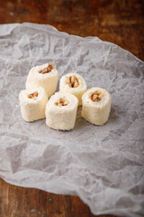 Turkish delight, white locum roll with walnut and coconut flakes on white paper, wooden background. Eastern sweets, oriental food. Traditional dessert