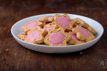 Star shaped cookies with pink frosting on white plate, wooden rustic background. Strawberry icing on cookies in shape of stars. Closeup