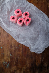 Turkish delight, pink and white locum roll with walnut and jelly on paper, wooden background. Eastern sweets, oriental food. Traditional tasty dessert