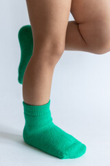 Legs of a 2 year old baby in warm green socks on a white background
