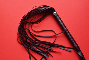 Leather black whip for sex games on a red background. BDSM toys for role-playing sex games.