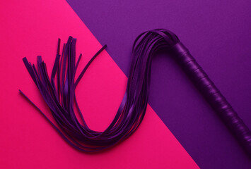 Leather black whip for sex games on a purple background. BDSM toys for role-playing sex games.