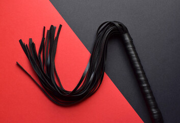 Leather black whip for sex games on red and black background. BDSM toys for role-playing sex games....