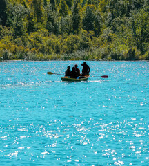 Four people enjoy a sunny day rowing on a vibrant turquoise lake surrounded by lush greenery