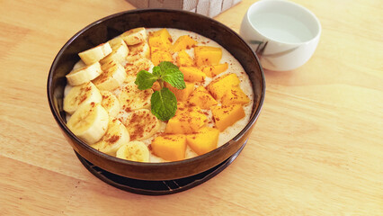Smoothie bowl with slices of bananas, mango, and mint on a light wooden table showing clean eating and healthy living to promote wellness
