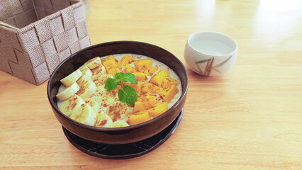 A smoothie bowl with banana and mango topped with mint leaves, set on a light wooden table, healthy vegan breakfast