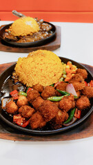 Fried tofu cubes and java rice served on a sizzling hot plate with mixed vegetables in a casual...