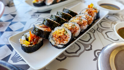 A plate of seaweed rice rolls or gimbap with vibrant fillings served on a patterned table, traditional local South Korean dish