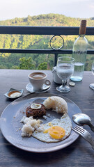 Half-eaten breakfast plate with fried egg, beef patty and rice on a table with an overlooking a lush green landscape, candid moment of a carefree daily life