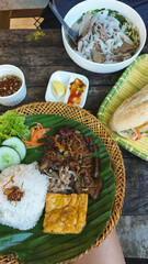 Authentic traditional local Vietnamese dishes featuring trung chien or egg omelet, thit heo nuong xa or grilled pork chop and rice on a banana leaf alongside pho bo or beef noodle soup and baguette