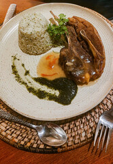 A plate of herbed rice and lamb chops with pesto sauce, artistically plated and presented on a woven placemat