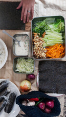 Hands set to prepare use seaweed sheet, surrounded by colorful vegetables, rice and other ingredients for making kimbap, traditional south korean food