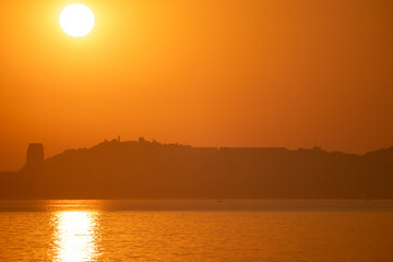 vibrant orange sunset over calm water and distant city