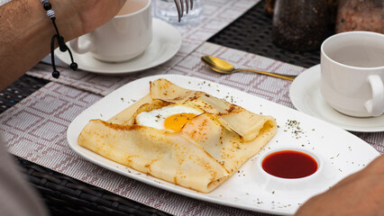 Close-up of a crepe with an egg and sauce alongside a cup of coffee on a woven table, healthy...