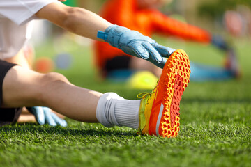 Youth Soccer Goalkeeper Stretching Before Game. Kid Warming Up with Gloves and Cleats on Football Field Grass