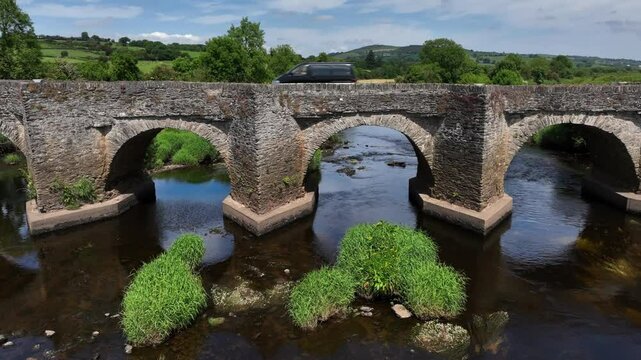 Clady Bridge, County Tyrone, Northern Ireland, June 2023. Drone slow ascend tilting down to establish arched bridge crossing over River Finn on a peaceful calm day.
