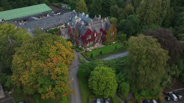 Hunting Lodge, Castle Leslie, Glaslough, County Monaghan, Ireland, September 2022. Drone angled approach along driveway to facade with red and green vegetation covering edge.