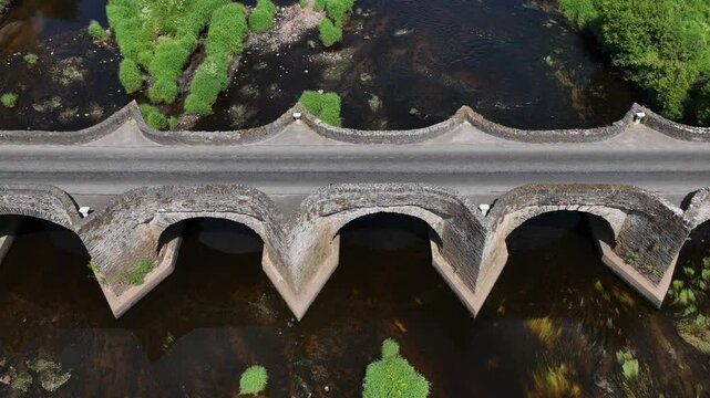 Clady Bridge, County Tyrone, Northern Ireland, June 2023. Drone ascend tilting down above arched bridge showcasing old historic architecture connecting villages.