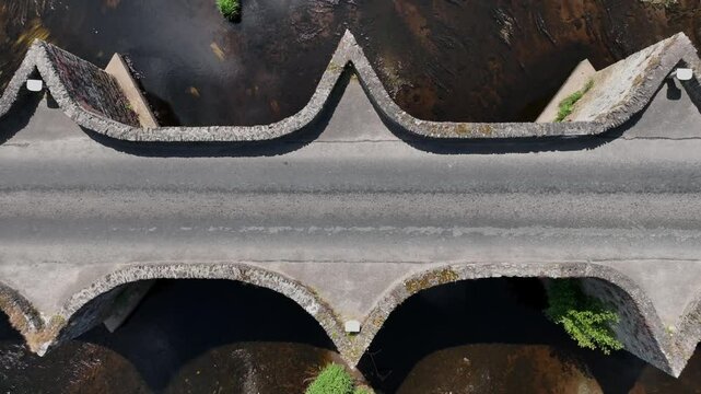 Clady Bridge, County Tyrone, Northern Ireland, June 2023. Drone symmetrical top down slow ascend bird's eye view above bridge crossing River Finn on a peaceful day.