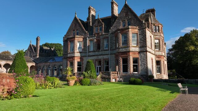 Castle Leslie, Glaslough, County Monaghan, Ireland, September 2022. Drone low approach over backyard lawn wall and manicured garden grass to rear entrance of castle.