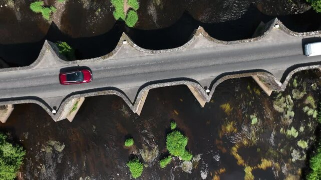 Clady Bridge, County Tyrone, Northern Ireland, June 2023. Drone top down bird's eye view approach and ascend orbit above arched bridge crossing River Finn.