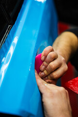 Detailing expert uses red squeegee wrapper to flatten blue PPF wrap on car surface. Vehicle wrap...