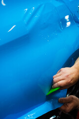 Applying a high-gloss blue PPF using a green squeegee ensures a bubble-free, smooth surface of car....