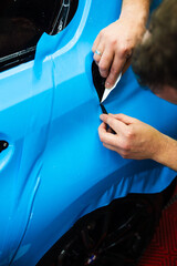 Detailing technician trims blue PPF on a car panel for perfect contour fit. Cutting blue PPF with...