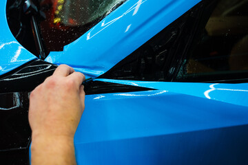 Detailing technician trims blue PPF on a car panel for perfect contour fit. Cutting blue PPF with...