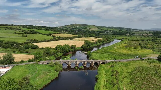 Clady Bridge, County Tyrone, Northern Ireland, June 2023. Drone medium orbit clockwise around arched bridge crossing River Finn connecting villages.