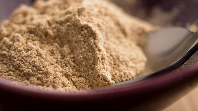 Bamboo spoon scoops up ground Ashwagandha root powder from a red ceramic bowl. Ayurvedic anti-stress remedy