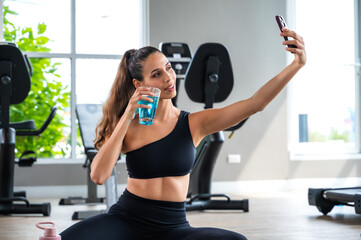 Active fitness woman holding healthy energy drink and selfie after doing exercise in house gym