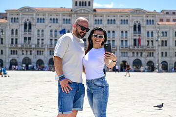 Naklejka premium Trieste ,Italy, Canal Grande .Happy smiling couple of tourists making photos near Canal Grande at Trieste .Concept of Italian gastronomy and travel. Italian couple having fun together 