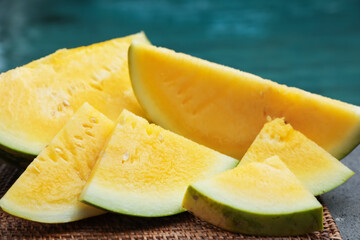 Pieces of ripe yellow watermelon on table near swimming pool, closeup